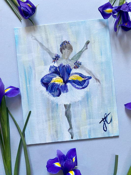 A painting of a ballerina in wearing an iris flower tutu. Photographed at an angle with fresh iris around the edges of the photo.