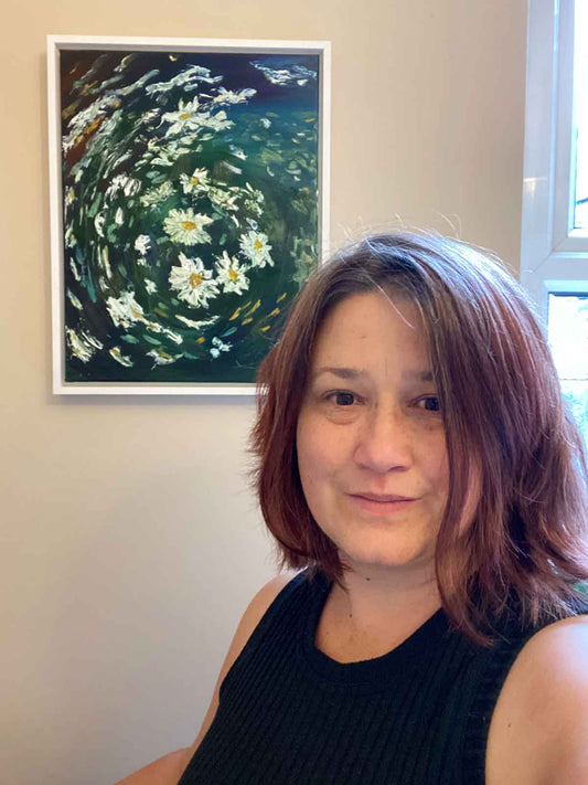 Selfie of Jeanne-Louise a woman with dark hair standing in front of a framed daisy painting