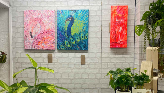 Display of 3 bright bird paintings in shop with plants