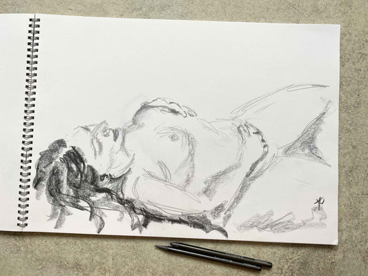 Graphite sketch of reclining female nude in sketchbook with graphite pencils