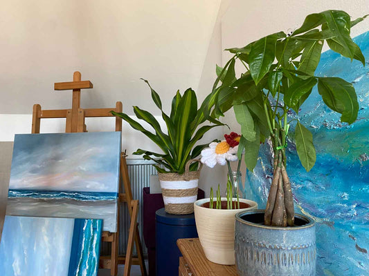 Art studio photo with seascapes against easel and 3 pot plants in front of another artwork