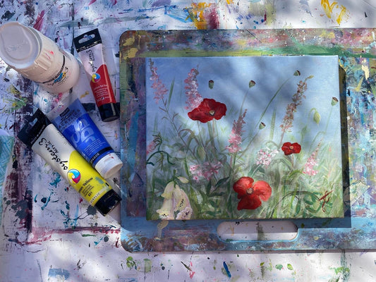 Plein air painting set-up with paint, boards and a flower painting. The light in the image is dappled.