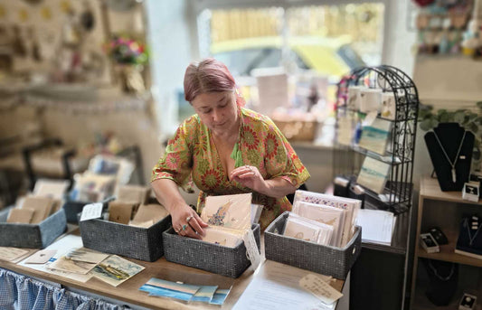 Woman seated in craft shop with display boxes with hand-created cards and art