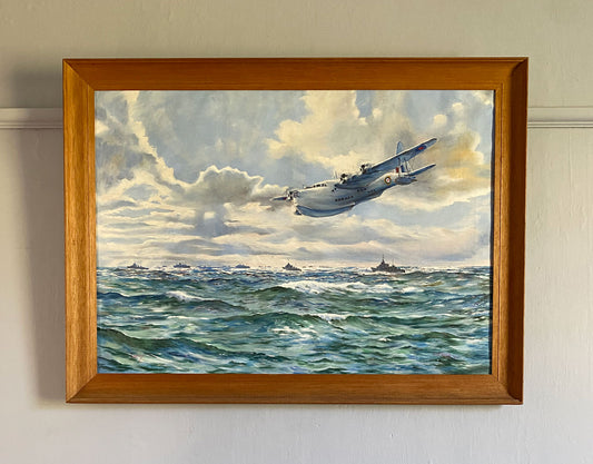 Painting of aeroplane flying over ocean with ships in the distance, framed and hung on a wall